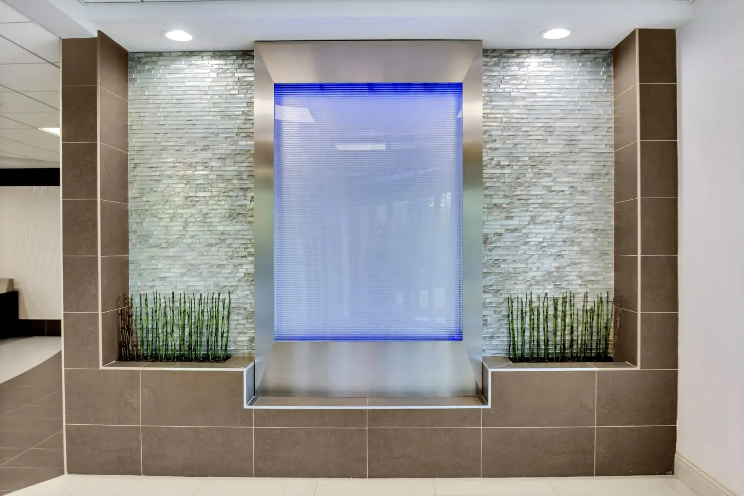 Backlit water wall framed in stone tile with bamboo planters