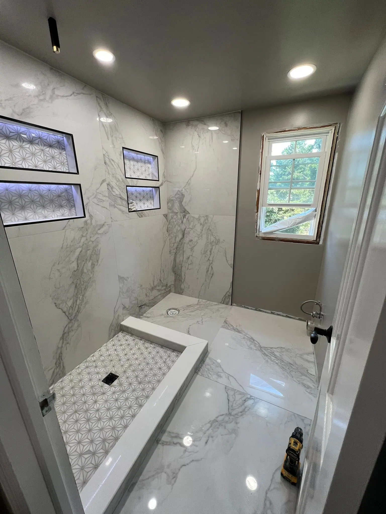 Finished bathroom with marble-look porcelain walls, curbless shower and lit niches